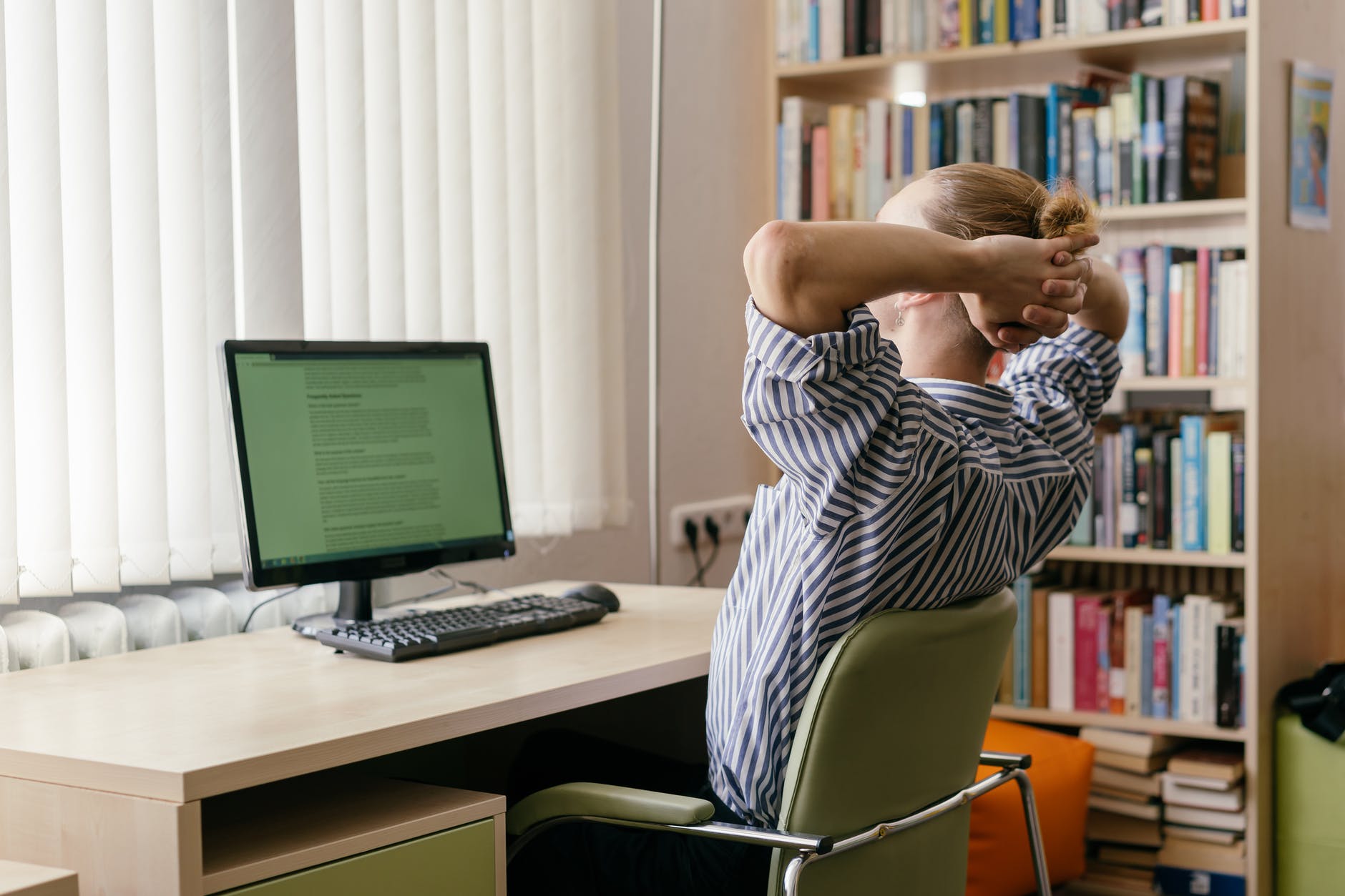 a man in striped shirt sitting on the chair while looking at the screen